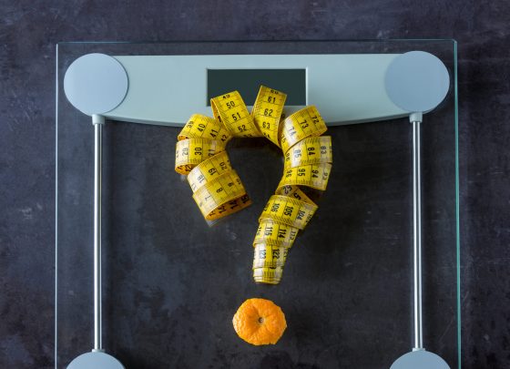 On the scales is measuring tape and fruit orange. Symbol-  question mark. Concept- lifestyle, sports and diet for weight loss.